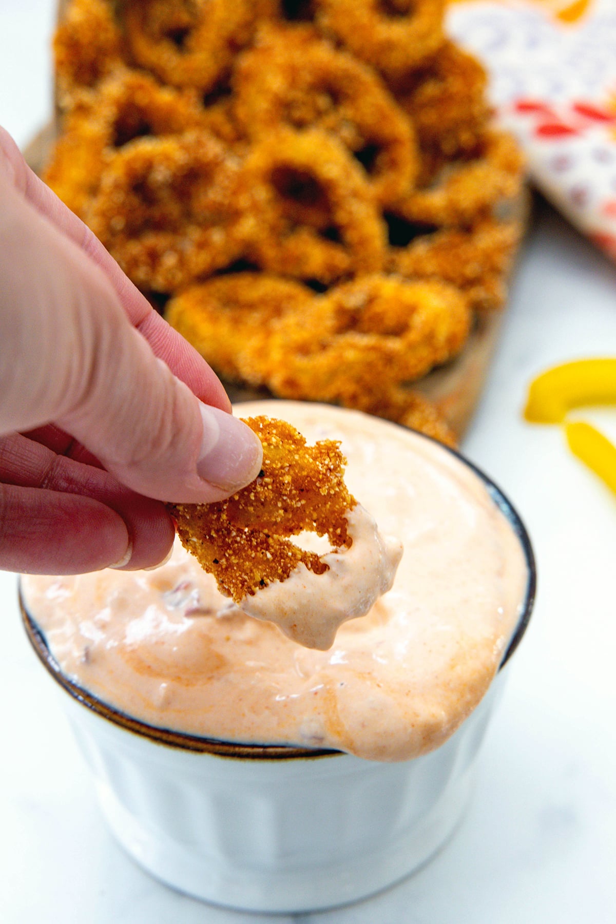 Fried banana pepper ring being dipped into sauce with more peppers in background.