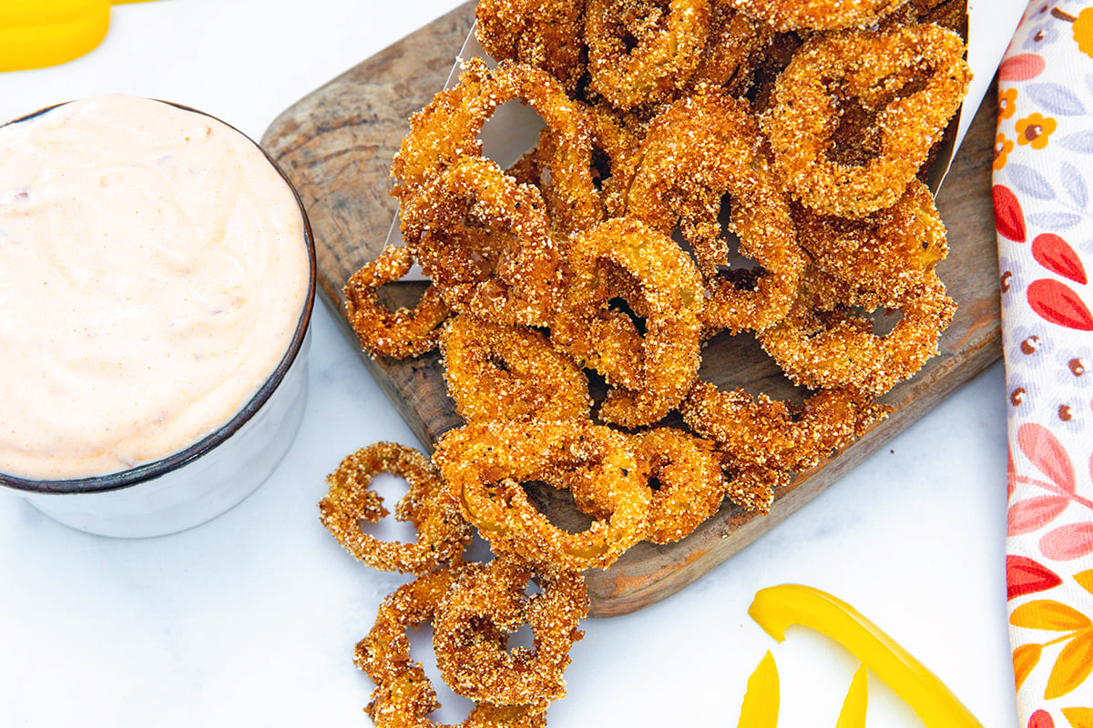 Landscape overhead view of fried banana peppers on wooden board with dipping sauce on the side.