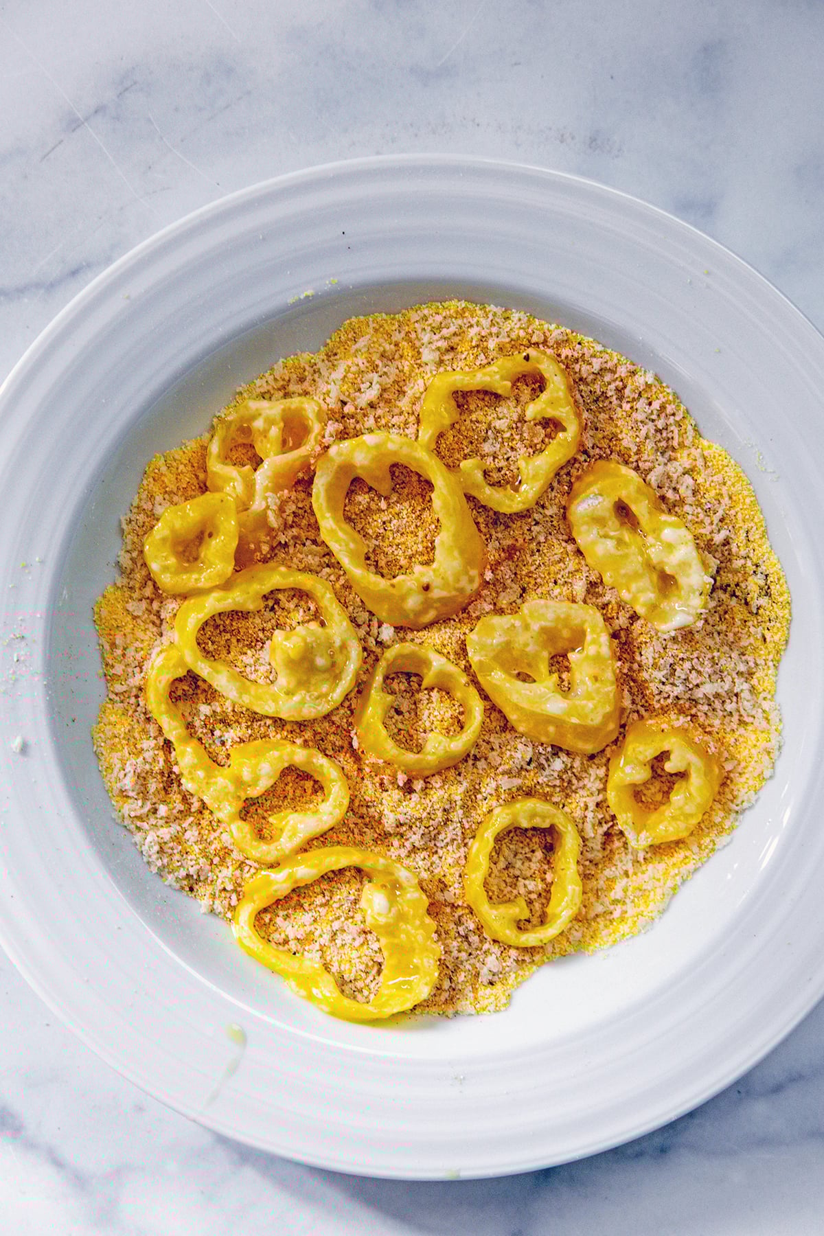 Floured and egg washed banana pepper rings in cornmeal.