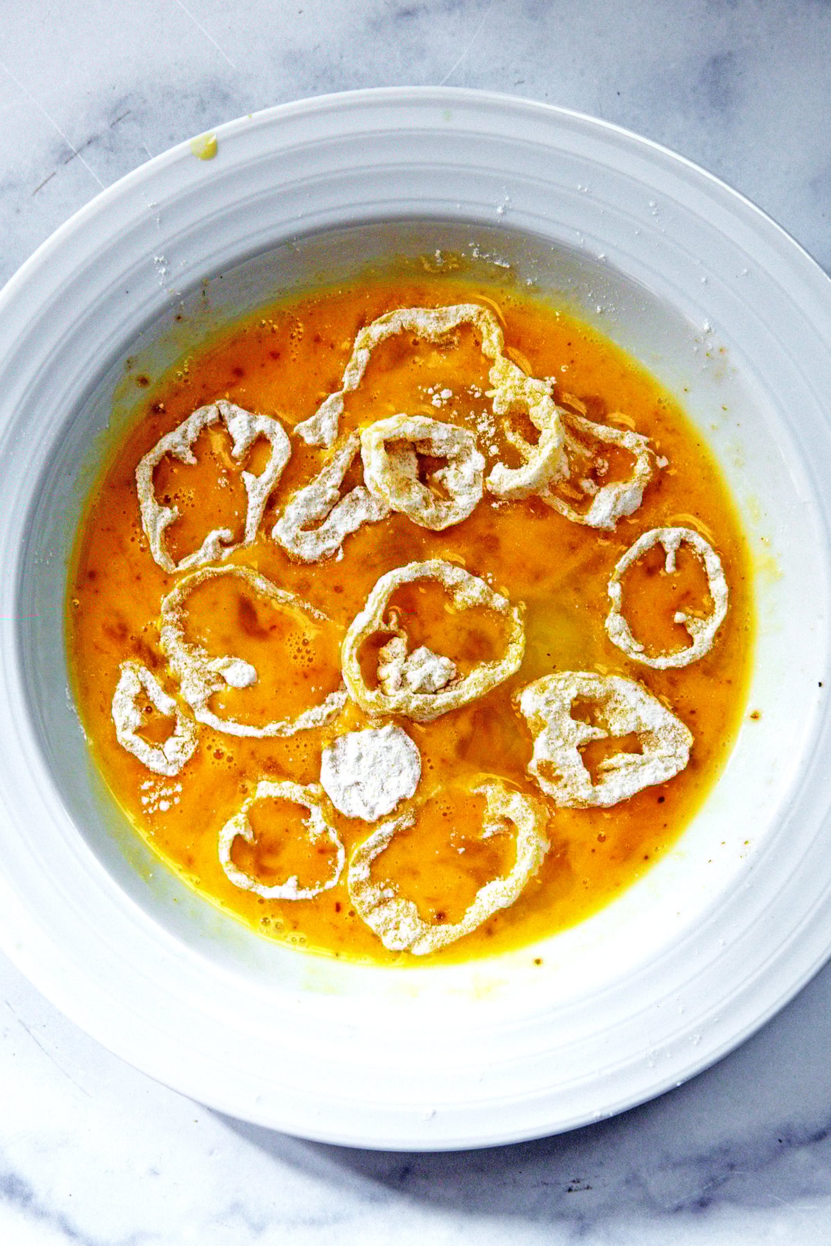 Banana pepper rings dipped in flour and sitting in egg wash.
