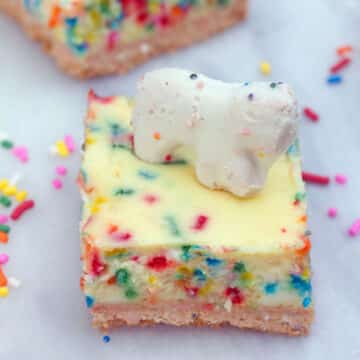 Closeup view of a frosted animal cracker cheesecake bar with white animal cracker on top and sprinkles.