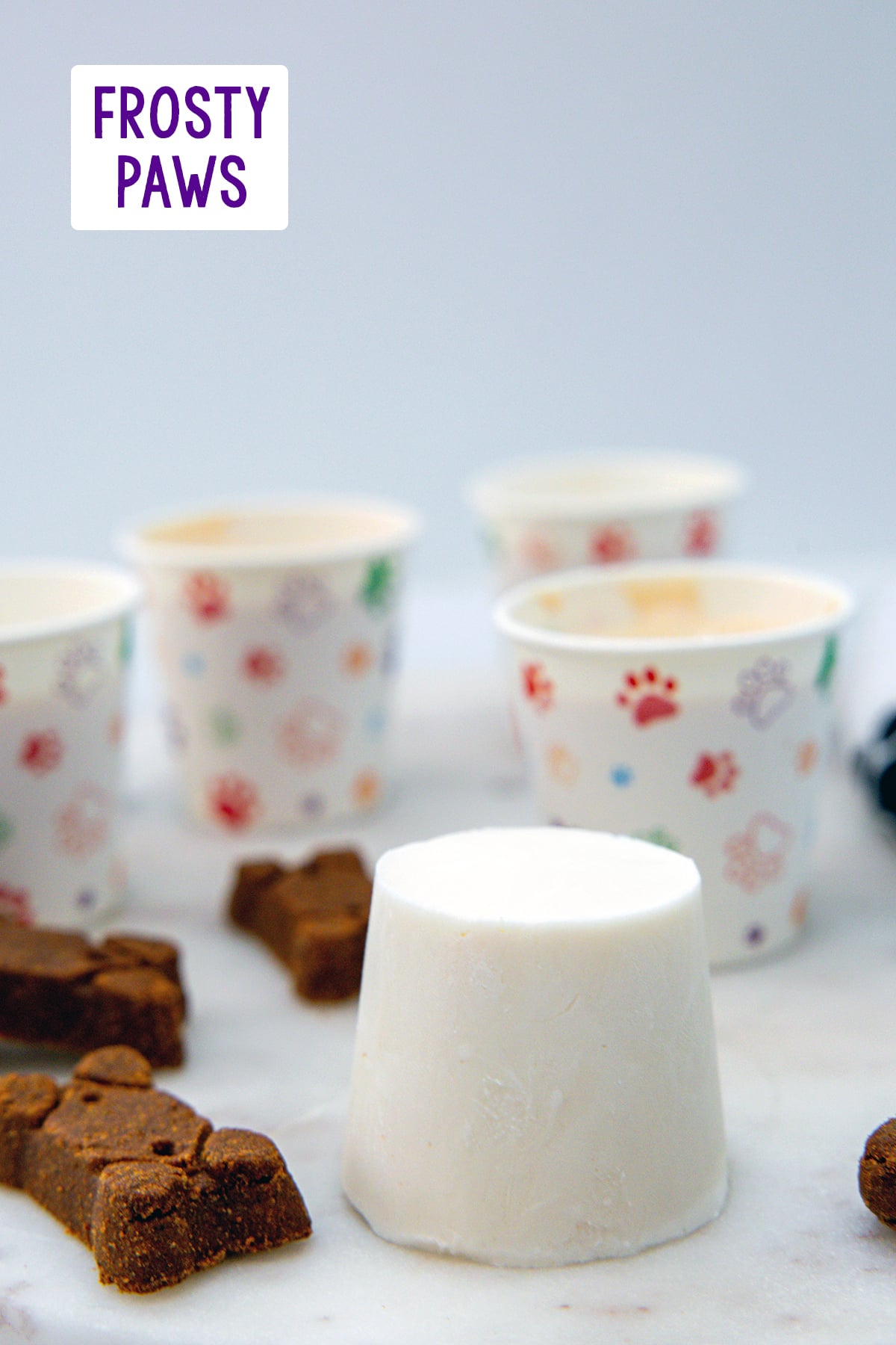 Head-on view of a homemade Frosty Paws ice cream with dog bones and more ice cream cups in background and recipe title at top.