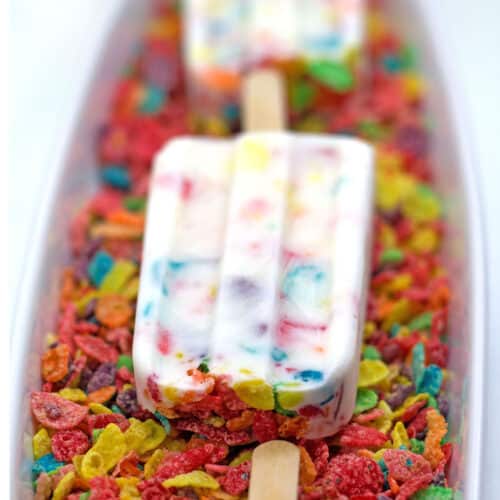 Closeup view of a Fruity Pebbles Greek yogurt popsicle on a bed of Fruity Pebbles.