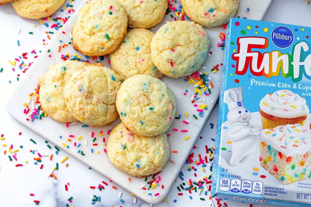 Landscape overhead view of Funfetti cake mix cookies with box of mix and rainbow sprinkles.