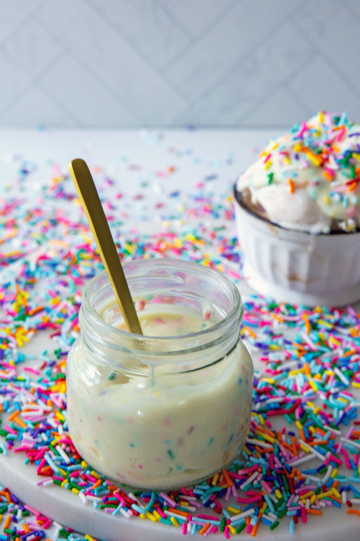 Funfetti magic shell in a small jar with spoon and rainbow sprinkles all around.