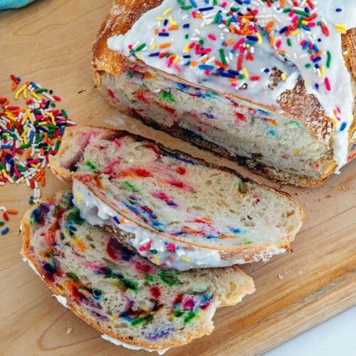 Overhead closeup view of slices of funfetti sourdough bread on a wood cutting board with rainbow sprinkles.