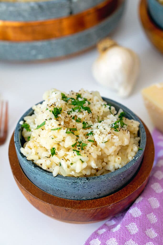 Bowl of garlic parmesan risotto topped with parsley with garlic bulb in background.