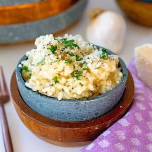 Garlic parmesan risotto in a small bowl with head of garlic in background.