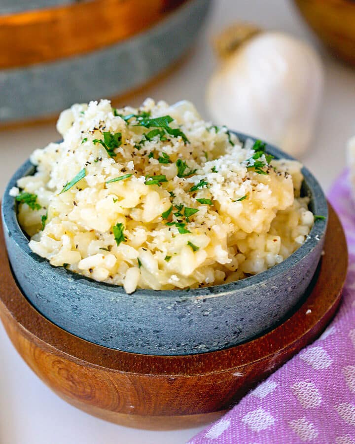 Garlic parmesan risotto in a small bowl with head of garlic in background.