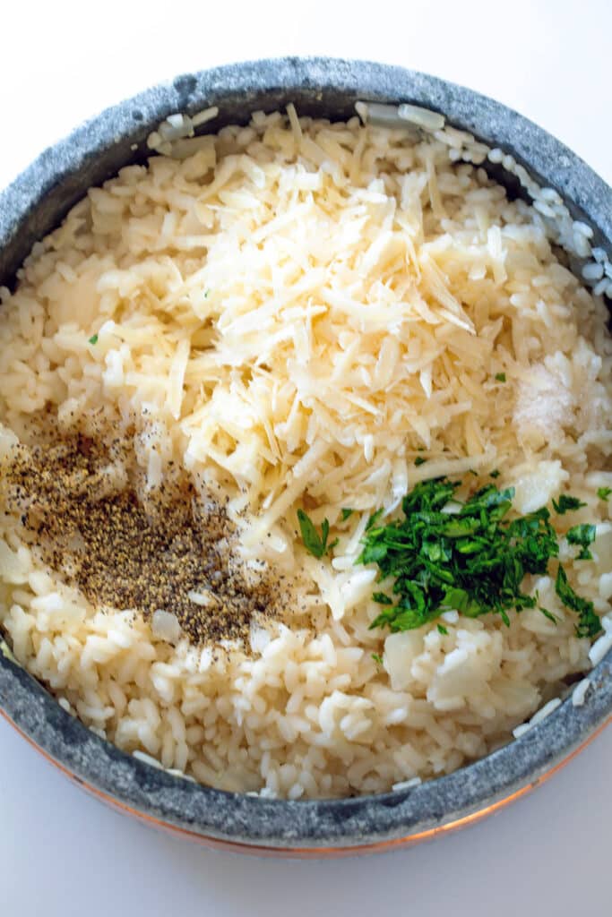 Parmesan cheese, parsley, and ground black pepper in risotto in pot.