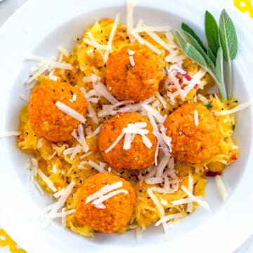Closeup view of pumpkin chicken meatballs on top of garlic spaghetti squash in a white bowl with sage.