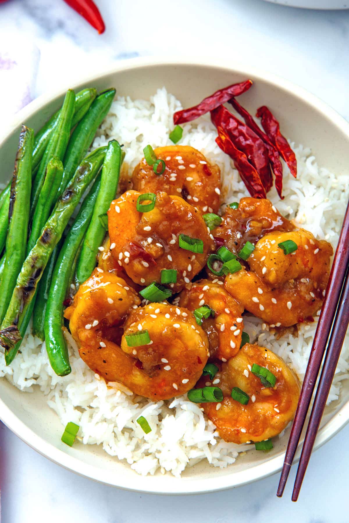 Closeup view of General Tso's shrimp over rice with green beans in bowl.