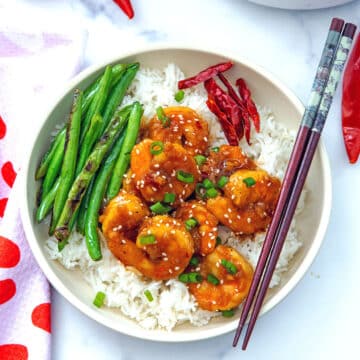 Closeup view of a bowl of General Tso's shrimp over white rice with green beans.