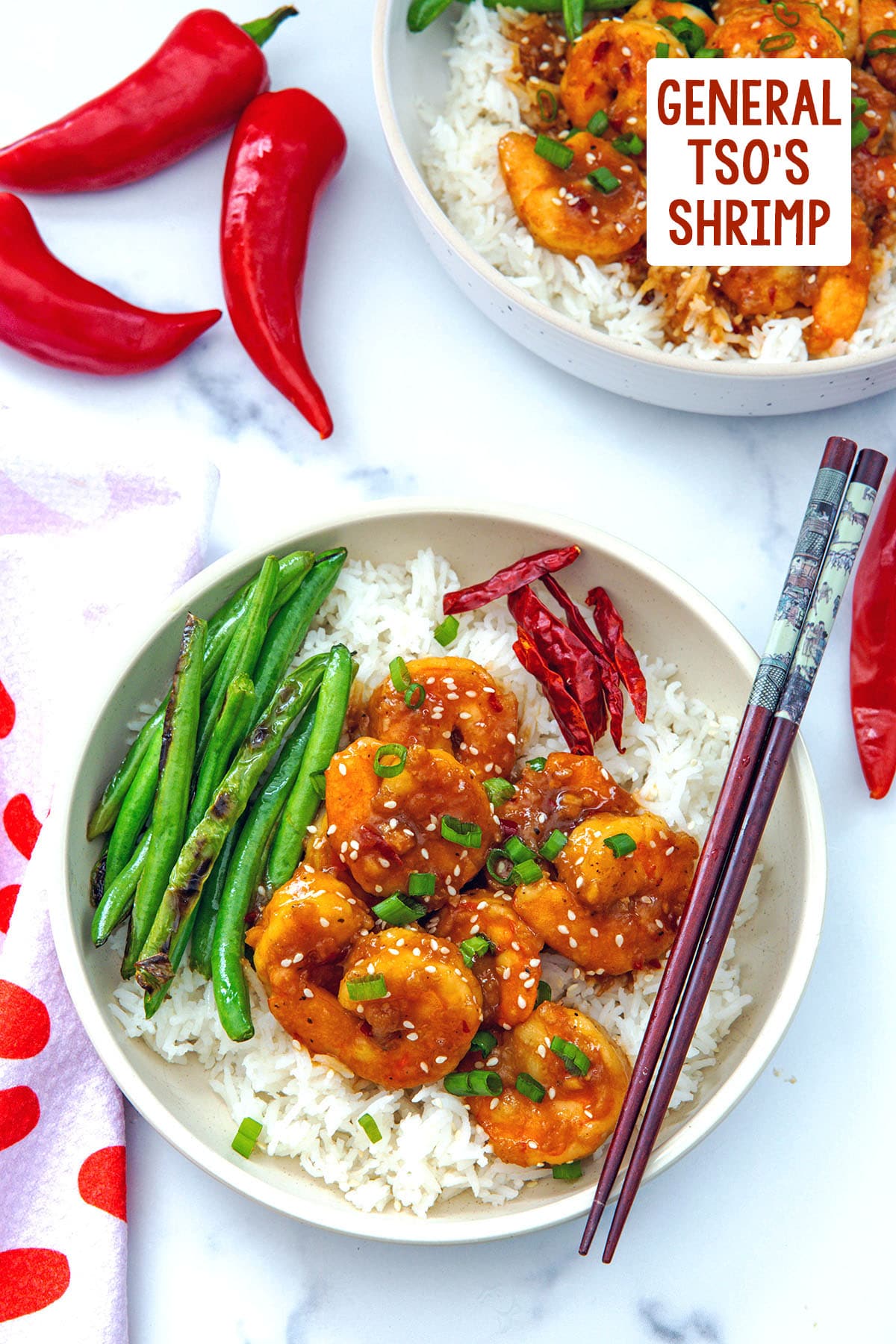 Overhead view of a bowl of general tso's shrimp over white rice with green beans with another bowl in background and recipe title at top.