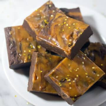 Closeup view of gingerbread chocolate caramel fudge with gold star sprinkles stacked on a plate.