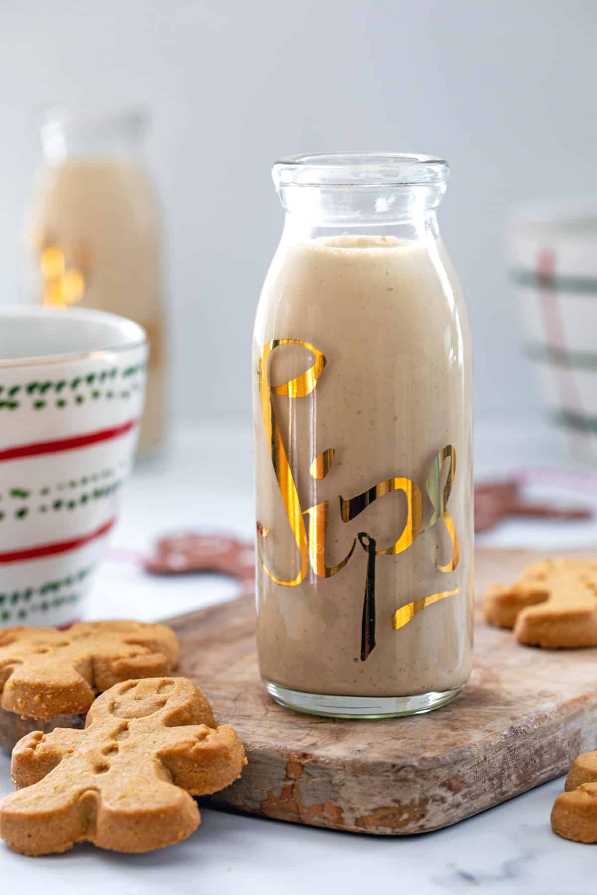 Head-on view of a carafe of gingerbread coffee creamer with coffee cups and gingerbread men cookies around.