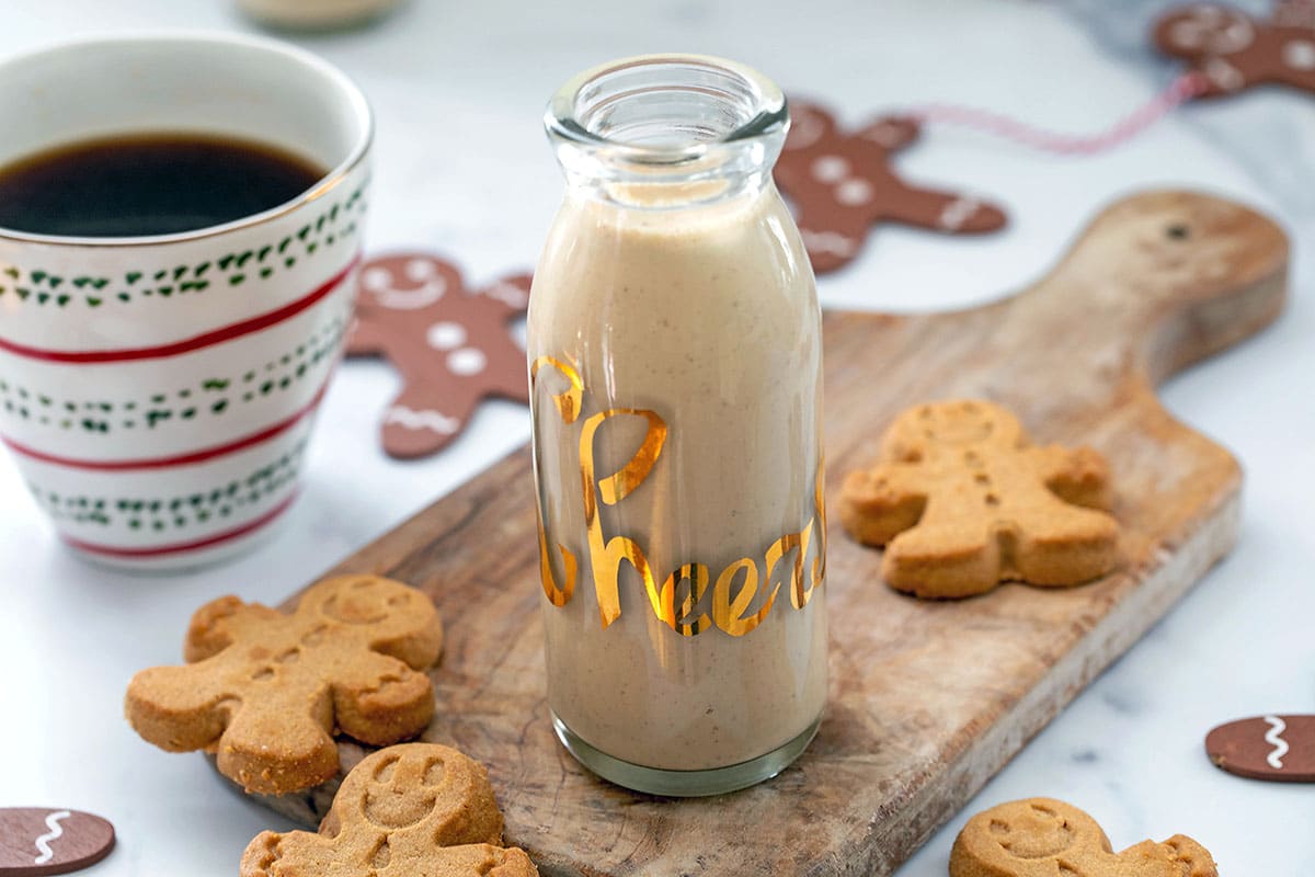 Landscape view of a small carafe of gingerbread coffee creamer with a cup of coffee and gingerbread men cookies in background.