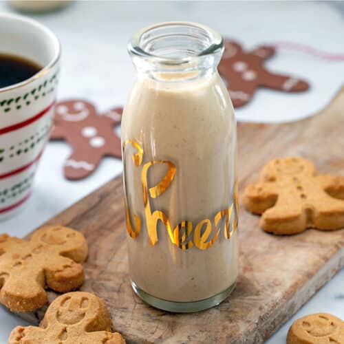 Small carafe of homemade gingerbread coffee creamer with gingerbread men cookies and cup of coffee.