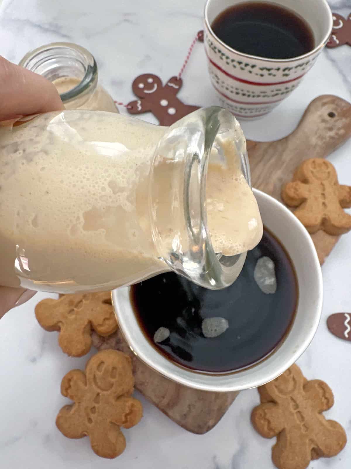 Overhead view of gingerbread coffee creamer being poured into a cup of black coffee with gingerbread men cookies all around.