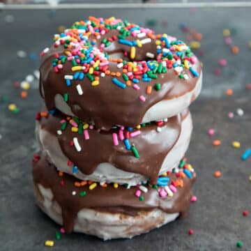 Closeup view of a stack of glaze chocolate donuts with chocolate frosting and rainbow sprinkles.