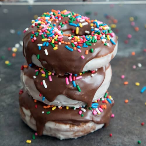 Closeup view of a stack of glaze chocolate donuts with chocolate frosting and rainbow sprinkles.