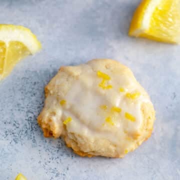 Overhead closeup view of a glazed lemon cookie with lemon wedges.