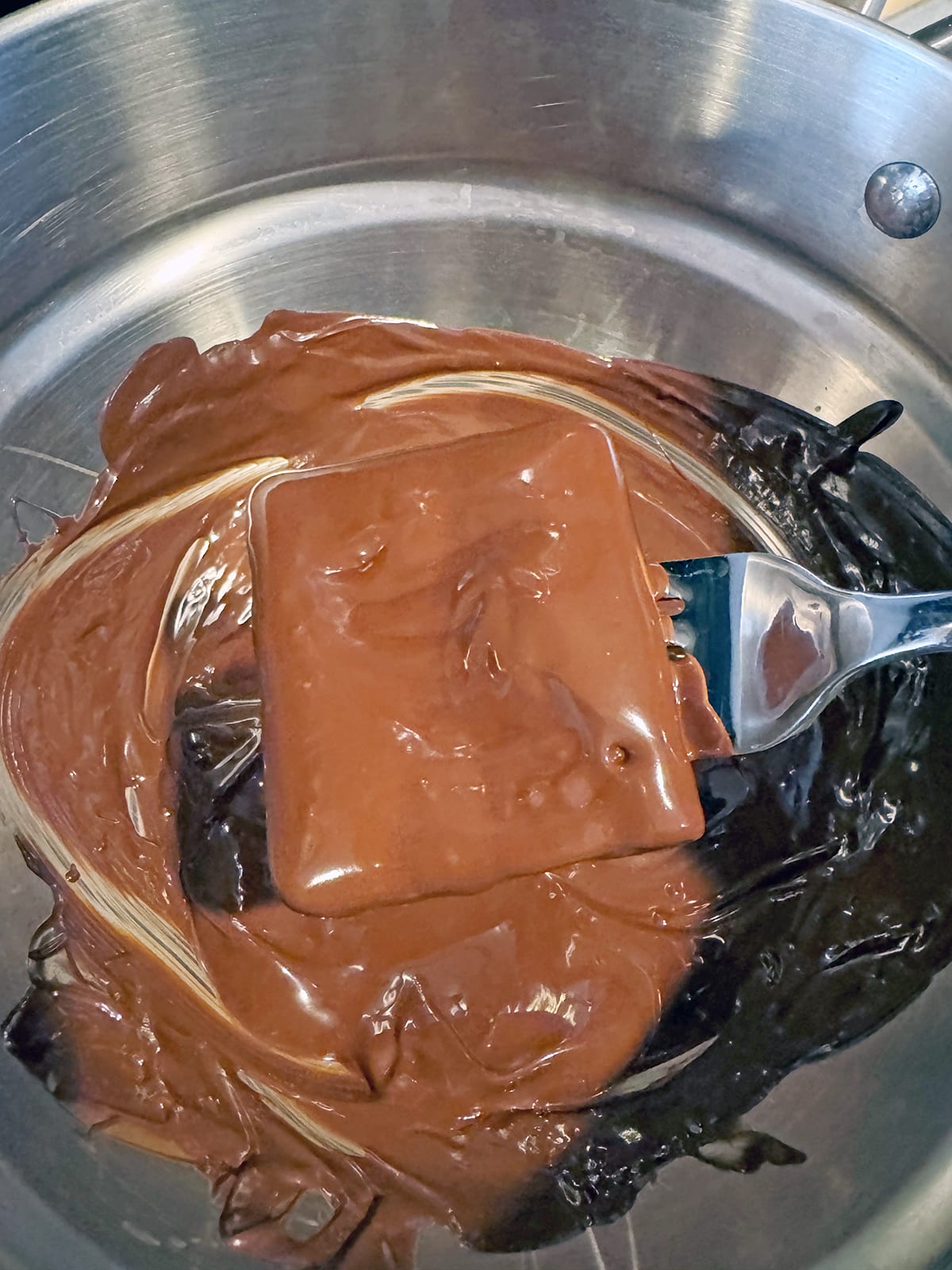 Chocolate covered graham cracker being lifted out of bowl with fork.