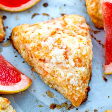 Closeup view of a grapefruit scone on a baking sheet with grapefruit wedges.