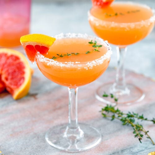 Closeup view of a grapefruit lillet cocktail with sprig of rosemary and grapefruit wedge.