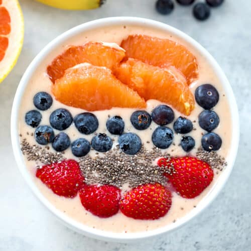 Closeup overhead view of a grapefruit smoothie bowl with grapefruit slices, blueberries, strawberry slices, and chia seeds.