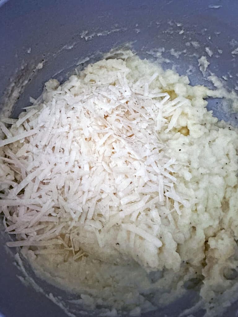 Grated parmesan cheese added to mashed potatoes in pot.