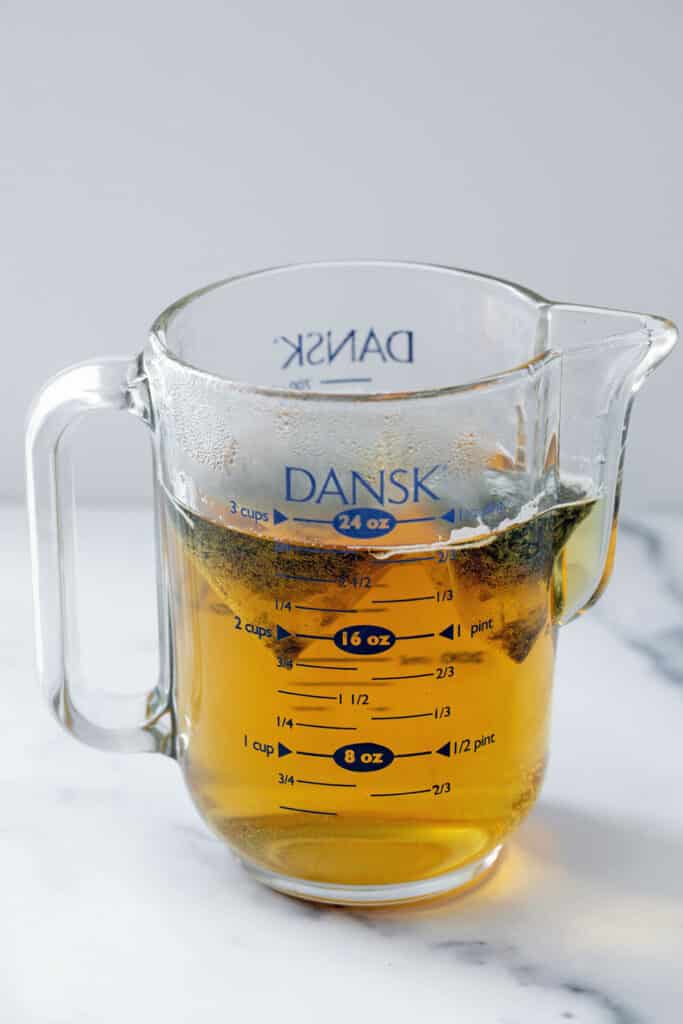 Green tea steeping in glass measuring cup.