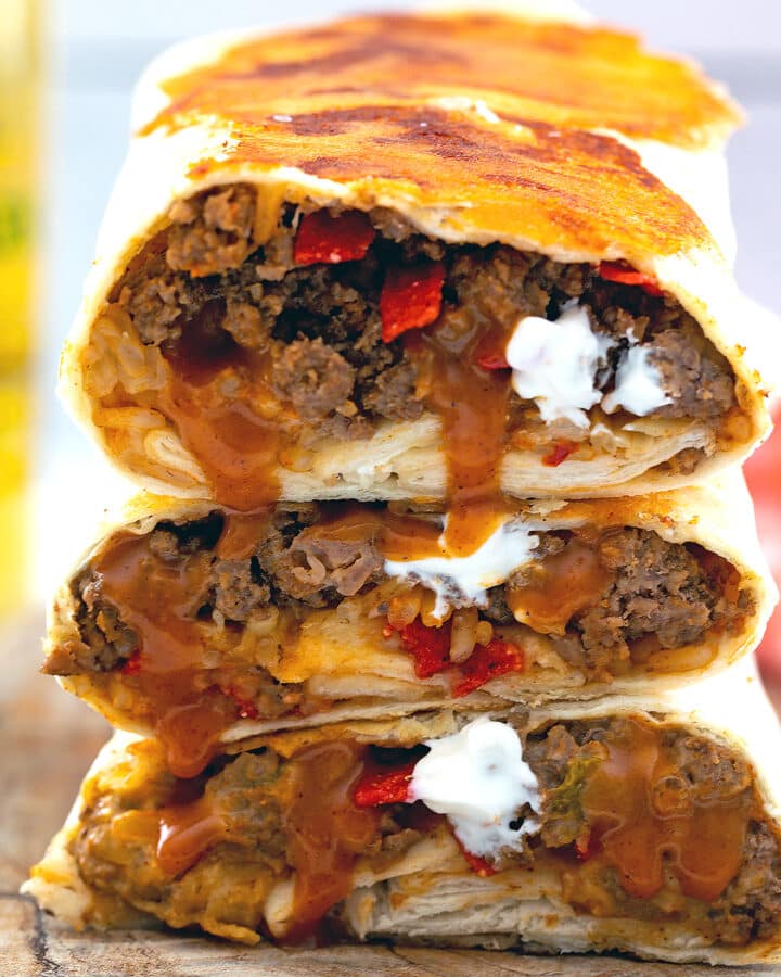 Closeup view of grilled cheese burritos stacked on each other with fillings.