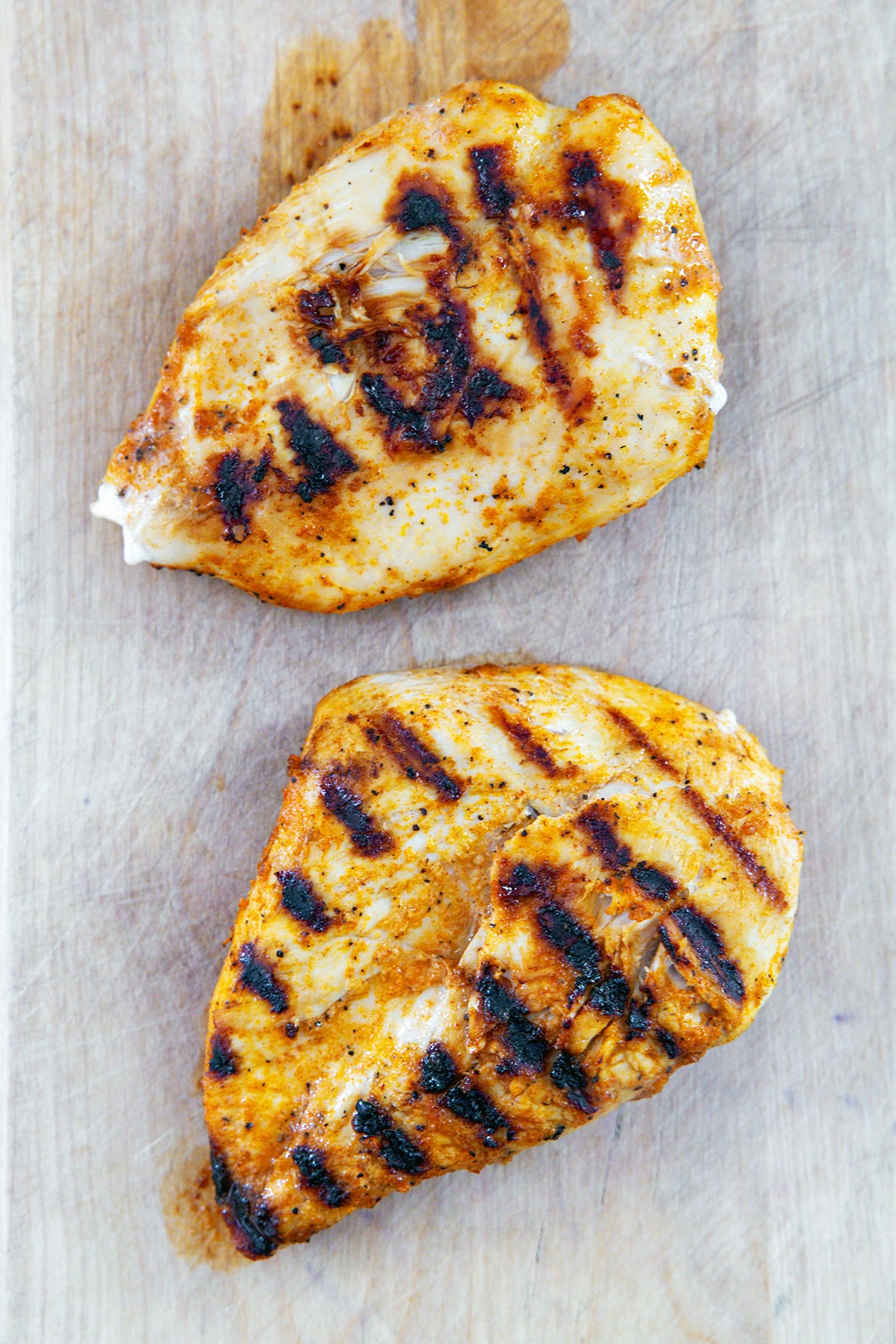 Two grilled chicken breasts on cutting board.
