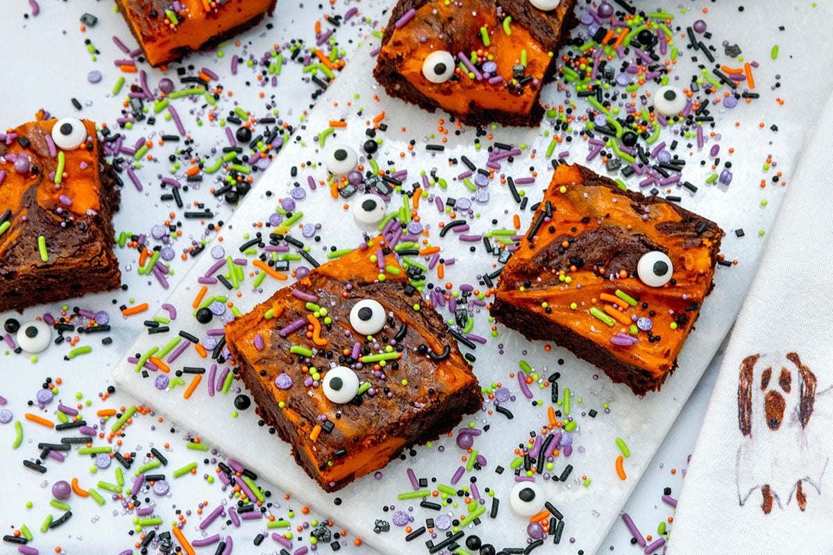 Landscape overhead view of multiple orange and black swirled Halloween brownies with lots of sprinkles and candy eyeballs.
