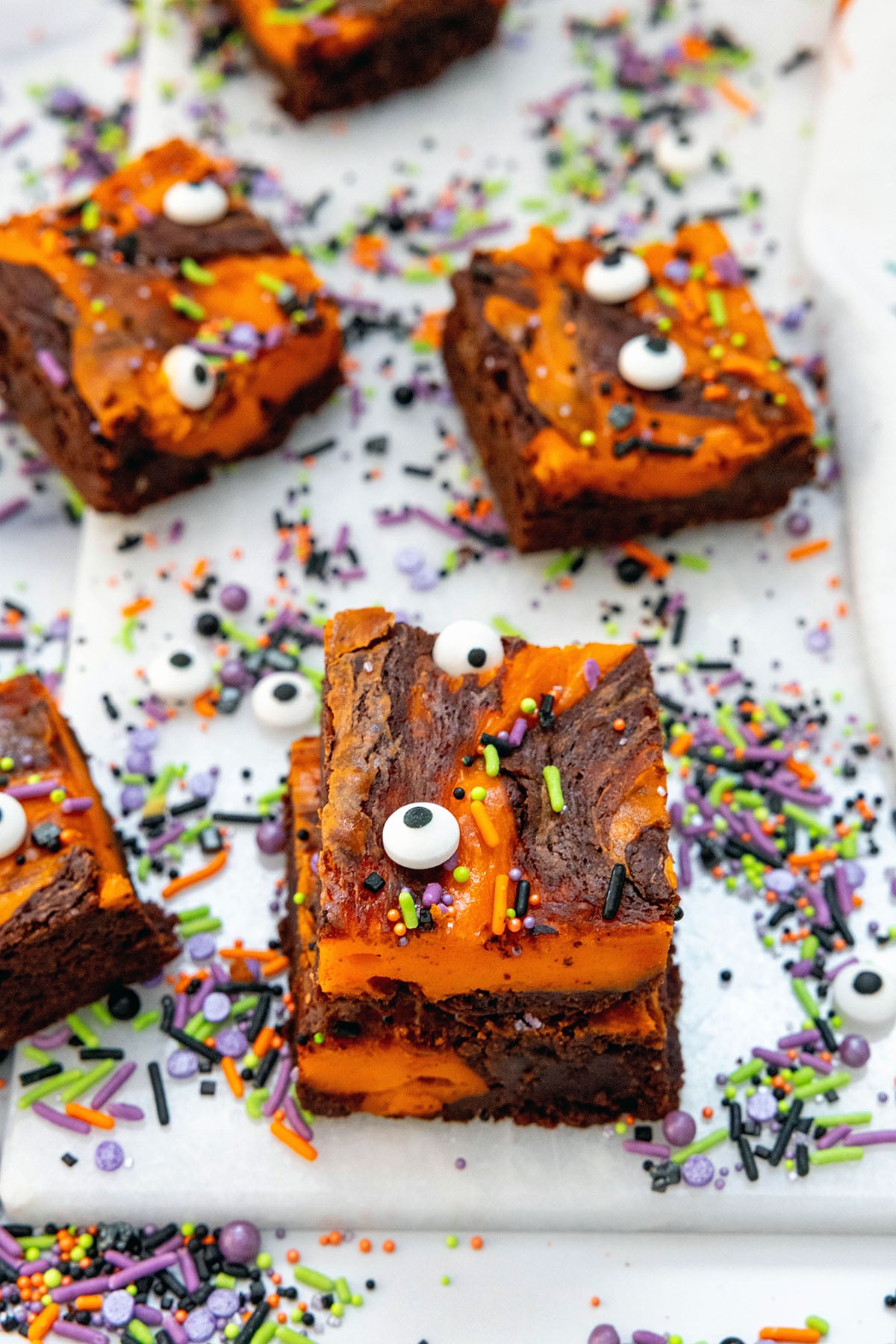 Mini stack of orange and black swirled Halloween brownies with sprinkles and candy eyes all around.