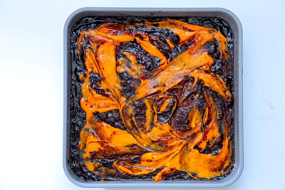 Brownie batter with orange cream cheese swirls in pan.