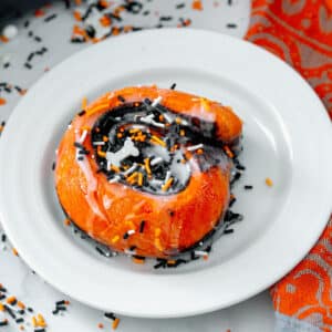 Closeup of orange Halloween cinnamon roll on a white plate.
