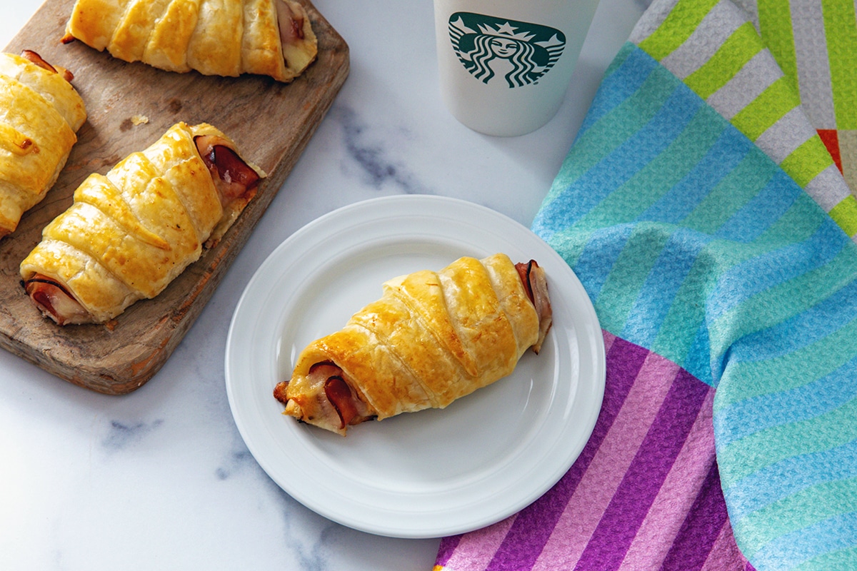Landscape overhead view of ham and cheese croissants with a Starbucks cup in the background.