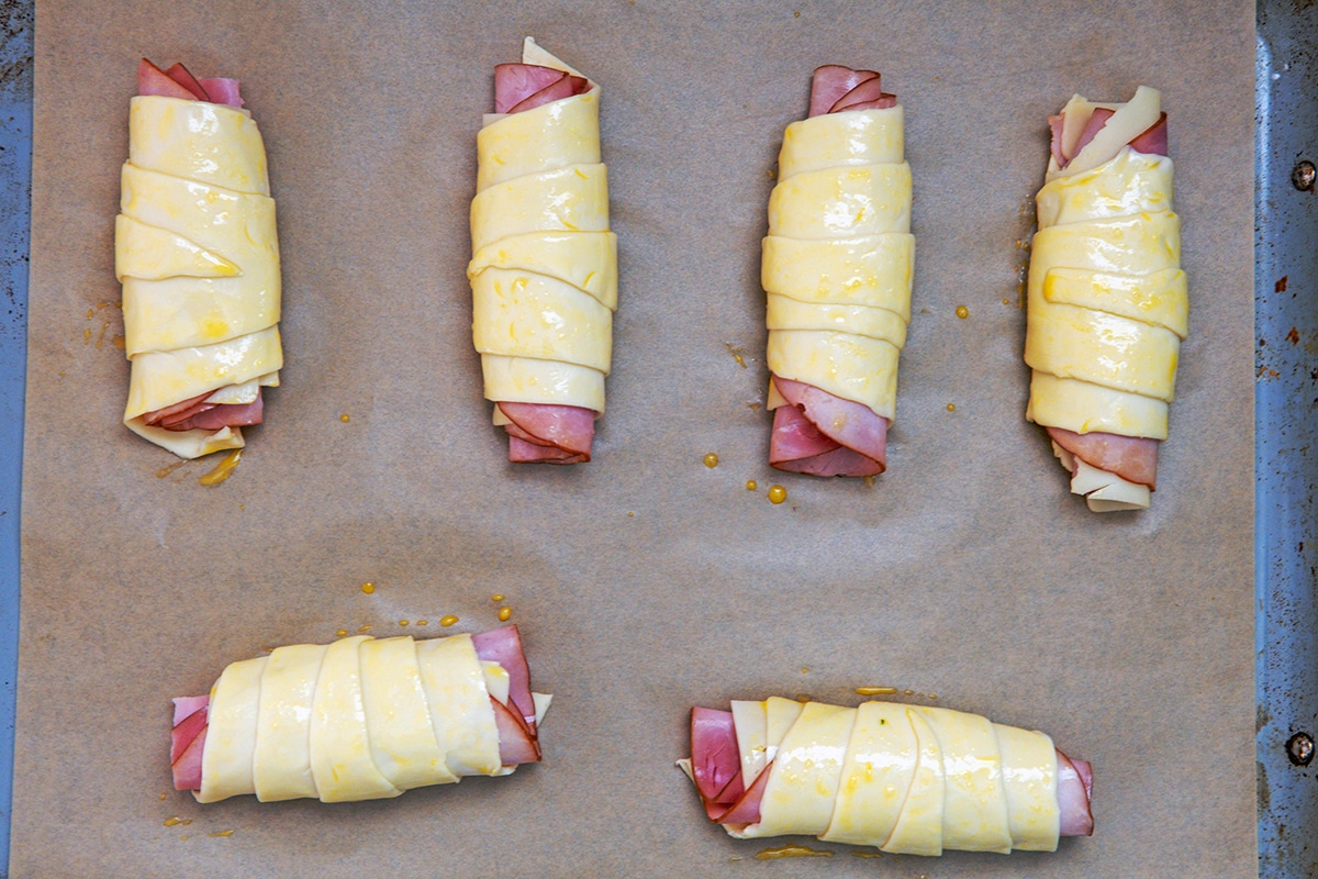 Landscape overhead photo of multiple ham and cheese croissants before they're cooked on a baking sheet.