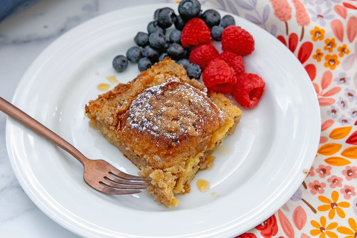 Landscape head-on view of a slice of Hawaiian roll french toast with berries and fork on plate.