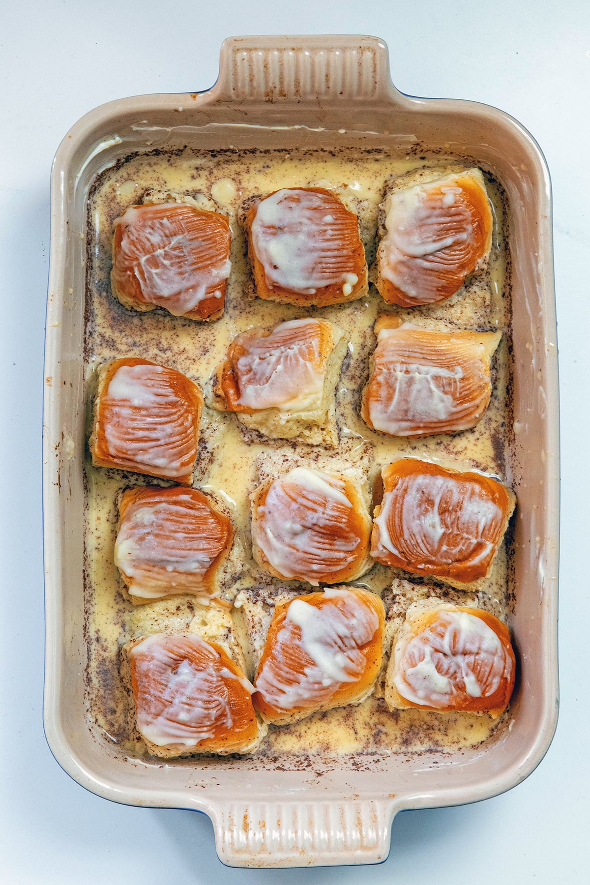 Overhead view of a casserole dish with Hawaiian rolls in custard mixture and topped with butter.