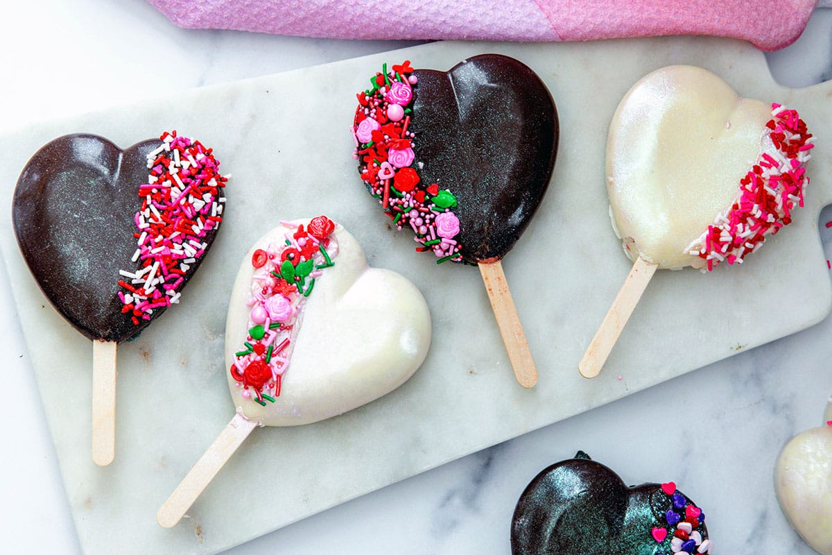 Landscape overhead view of chocolate and white chocolate heart-shaped cakesicles on marble surface.