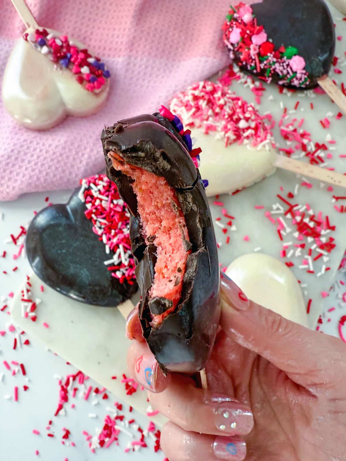 Chocolate cakesicle with bite taken out of it to show strawberry cake.