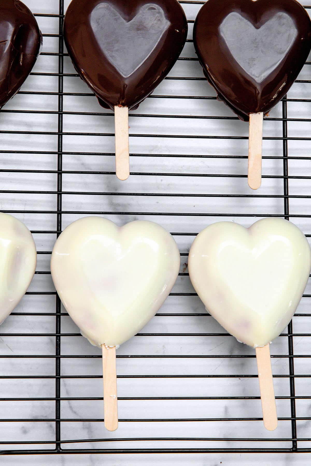 White chocolate and dark chocolate heart cakesicles on metal rack.