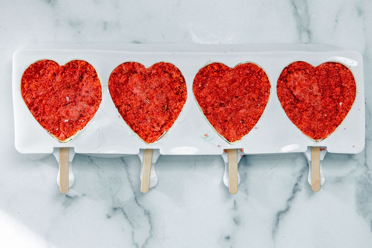 White chocolate coated heart molds with pink strawberry cake stuffed in them and popsicle sticks in them.