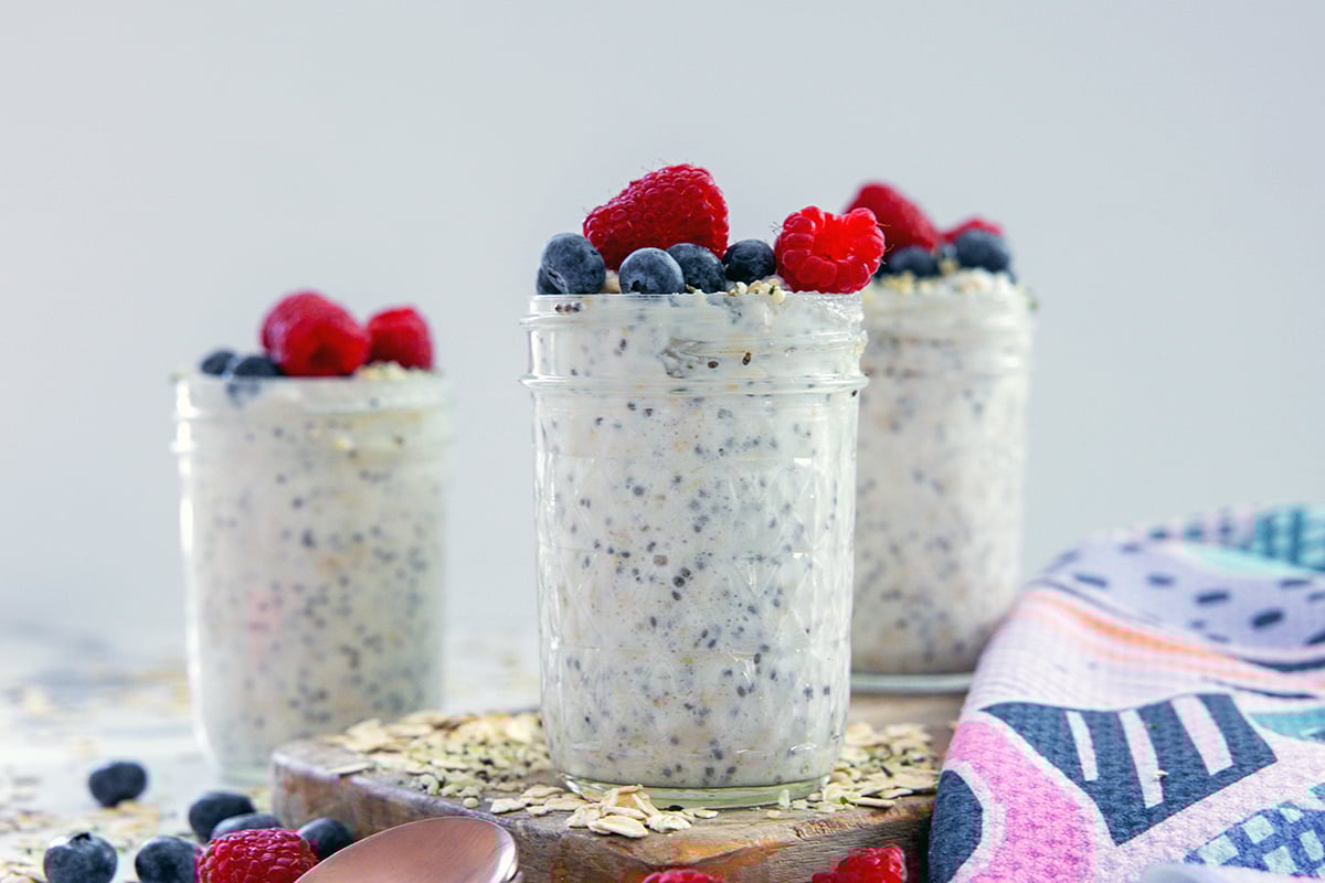 Head-on landscape view of three jars of high-protein overnight oats with oats and berries all around.