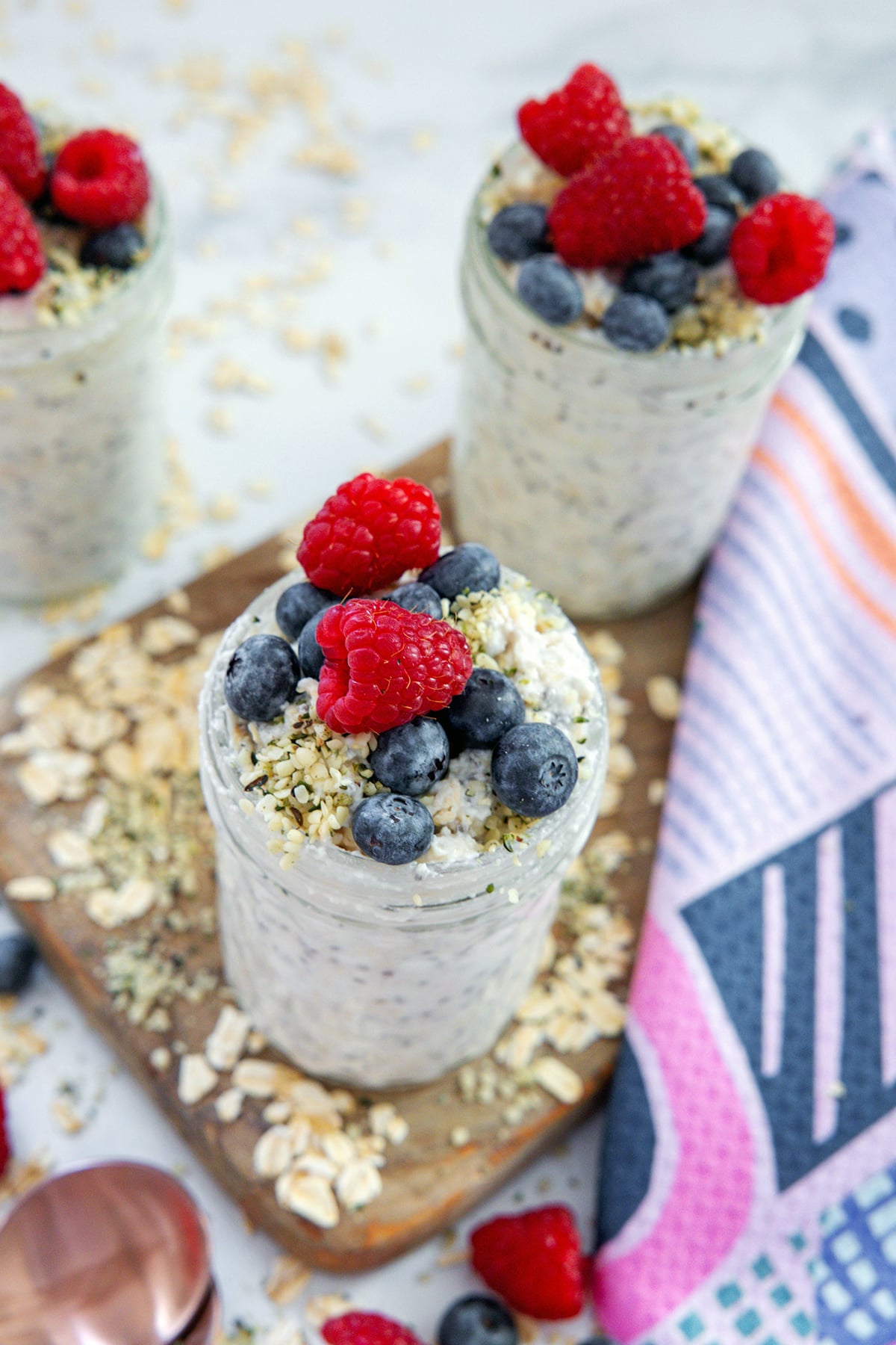 Overhead view of two jars of high-protein overnight oats with berries and hemp hears on top and oats all around.