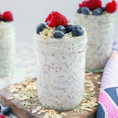 Closeup head-on view of a jar of high-protein overnight oats with berries and hemp hearts on top.
