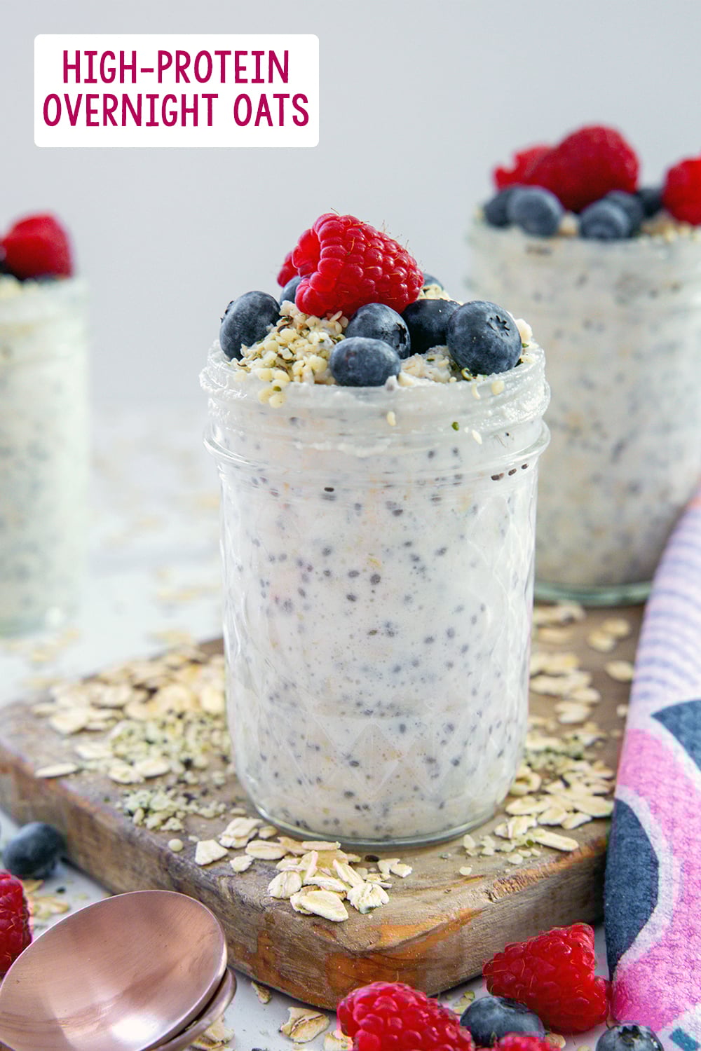 Head-on view of a jar of protein overnight oats topped with berries and more jars in background with recipe title at top of photo.